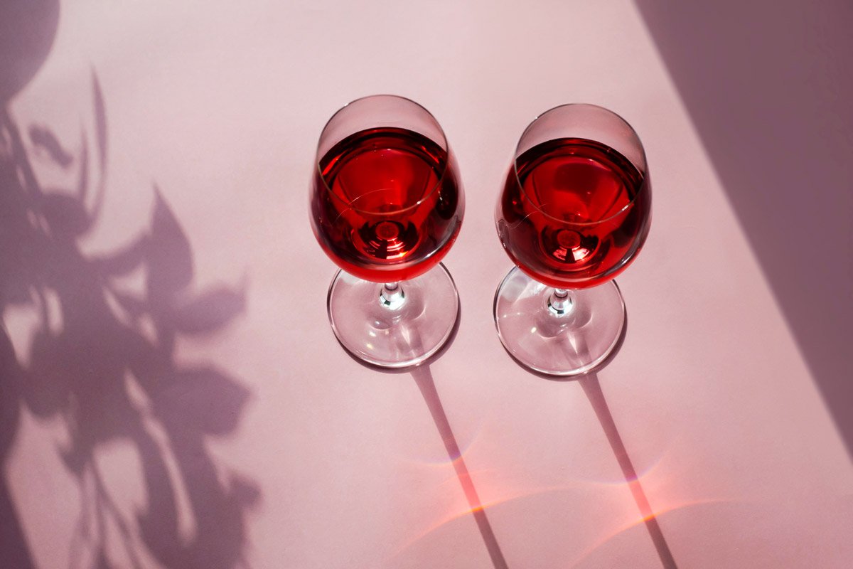 Two glasses of red wine sit on a purple background. 