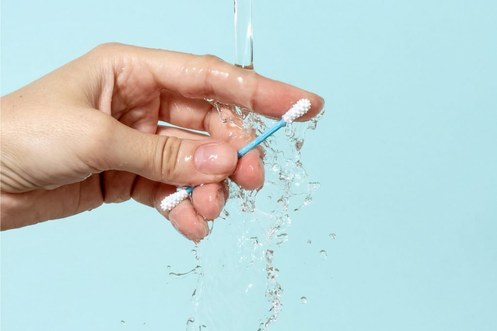 A reusable cotton swab is cleaned underneath water. 