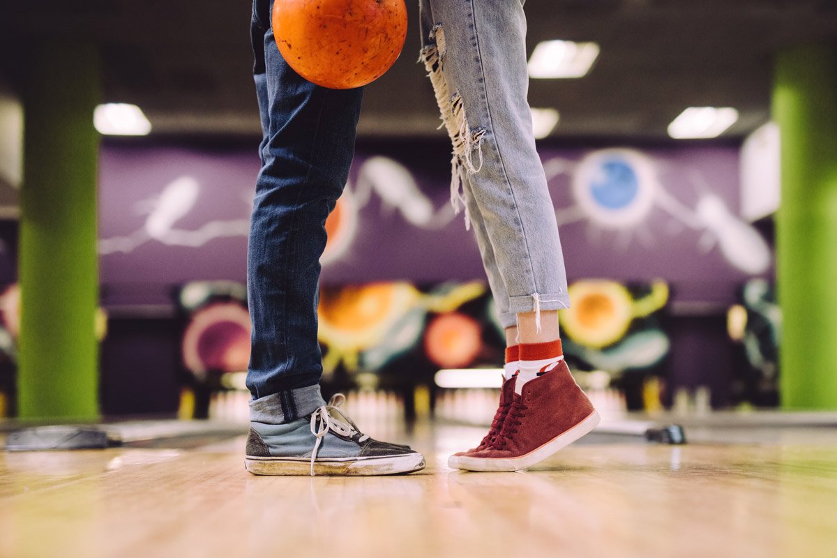 A couple stand next to each other while one holds a bowling ball at a bowling alley. 