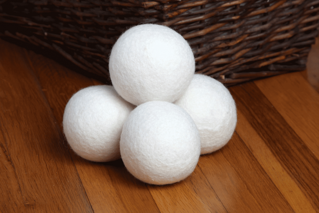 Three dryer balls sit next to a wicker basket on a wooden surface.