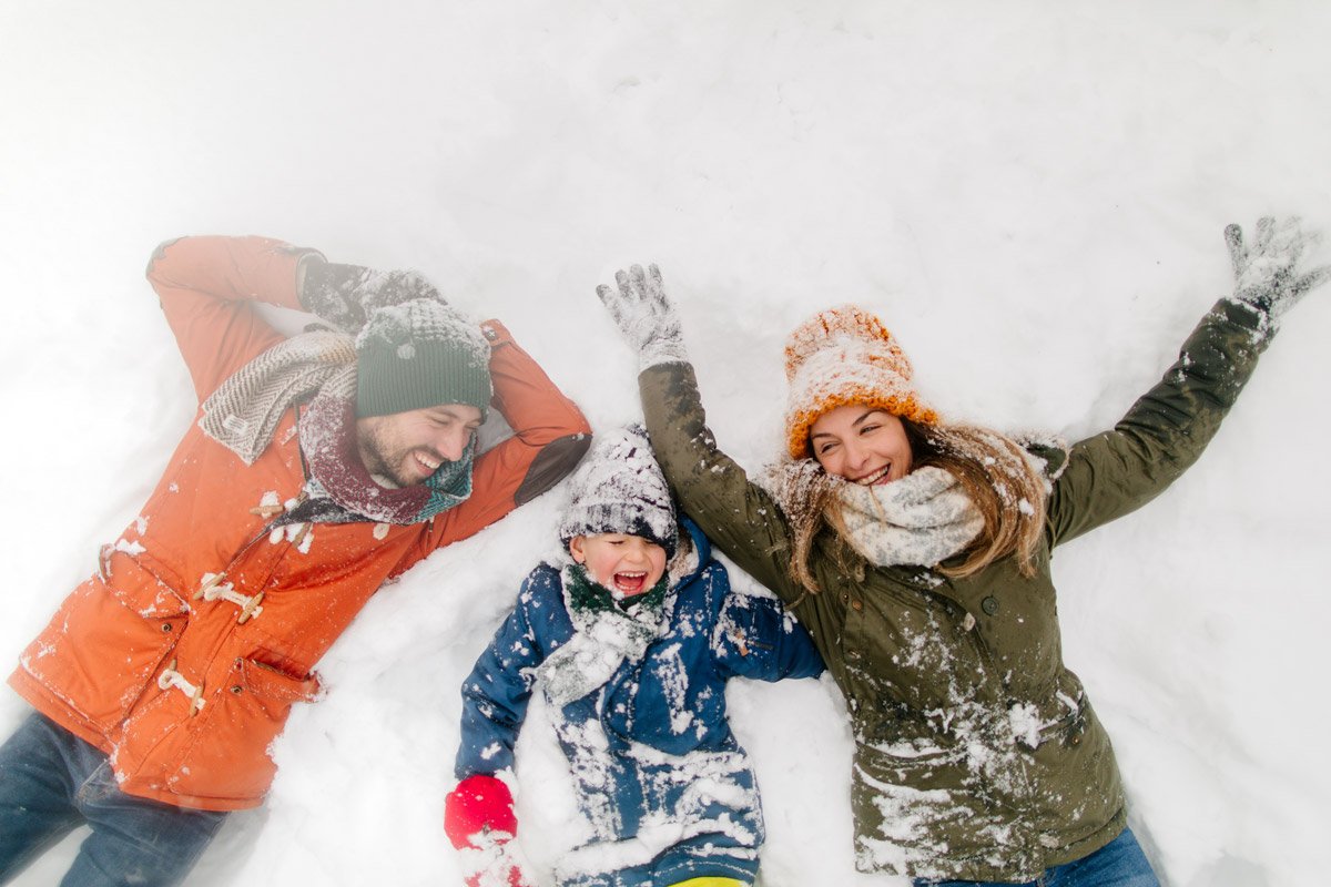 A family make snow angles in the snow while laughing. 