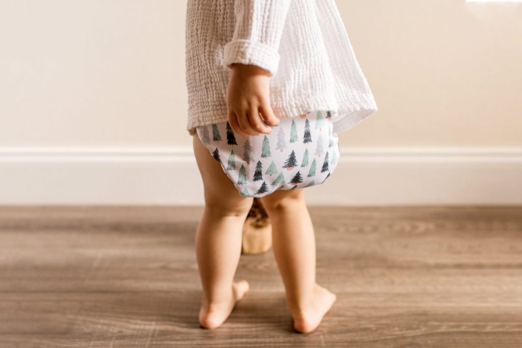 A toddler wears a cloth diaper while holding a stuffed animal. 