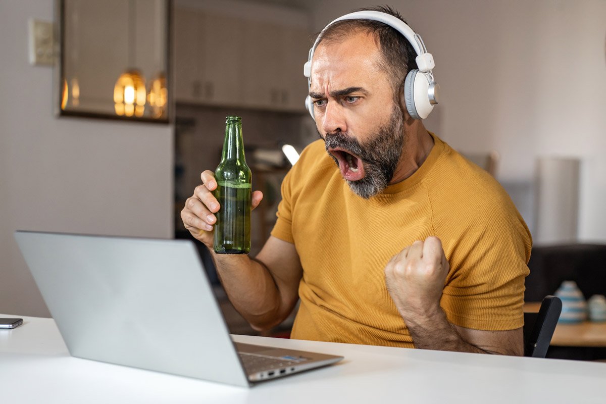 A man celebrates while watching football on his laptop. 