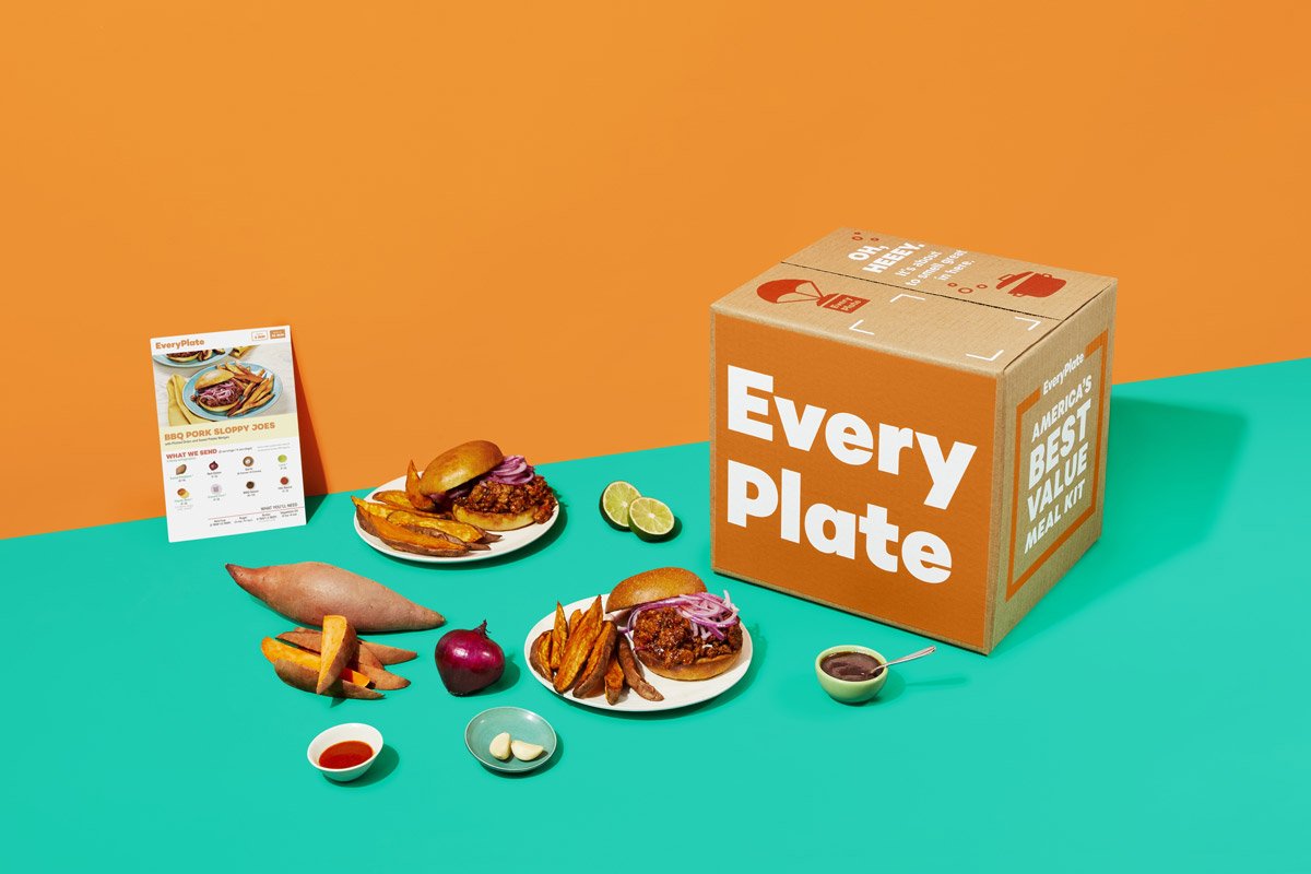 A box with the EveryPlate logo sits on a backdrop with sweet potatoes, a sandwich and condiments.