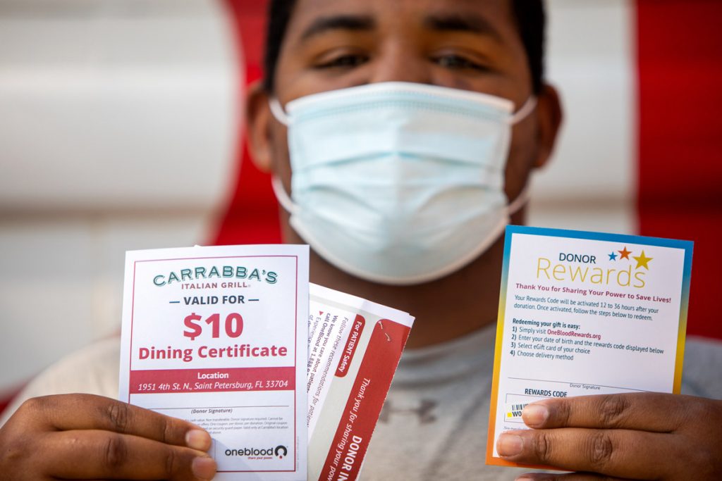 A man wearing a face mask shows off his gift certificates after donating blood.