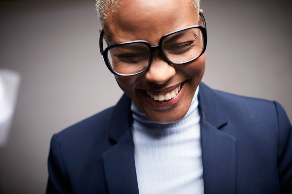 A woman laughs while wearing eyeglasses. 