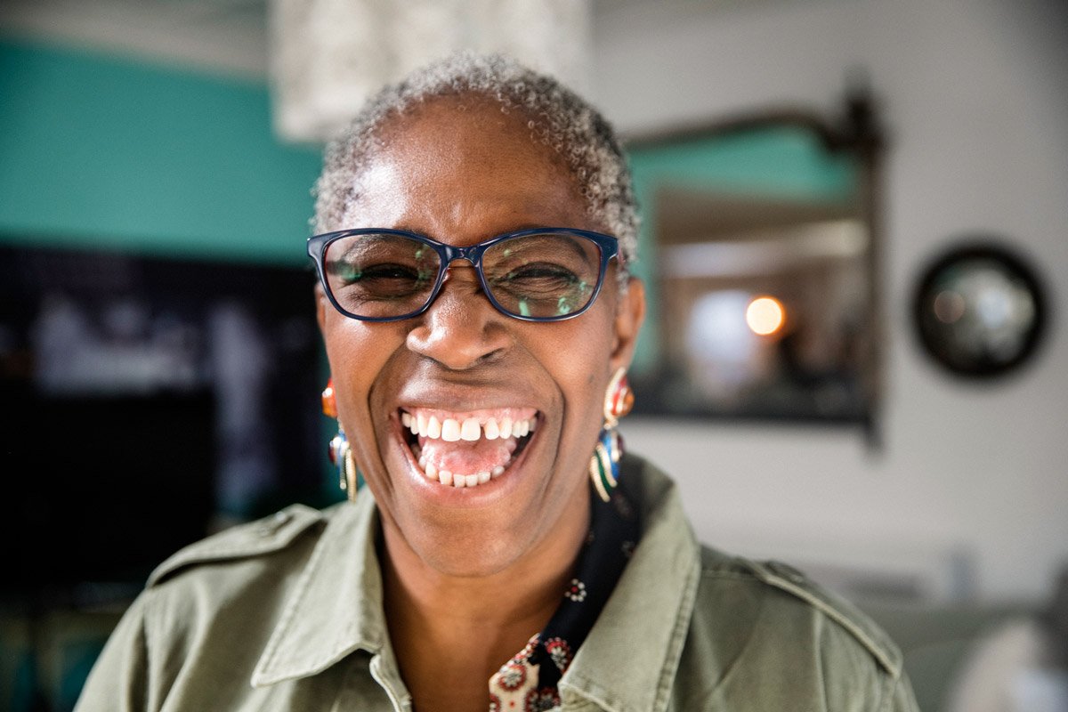 A woman laughs while wearing black framed eyeglasses. 