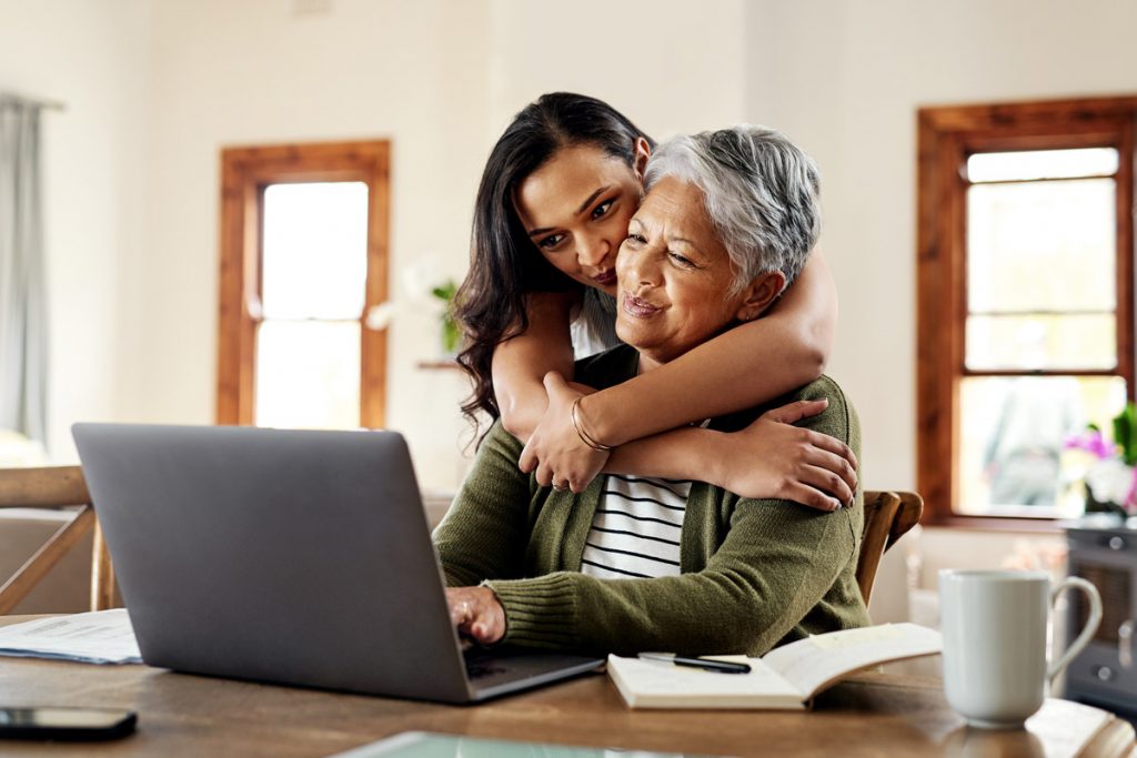 A daughter hugs her mother while she's on her laptop.