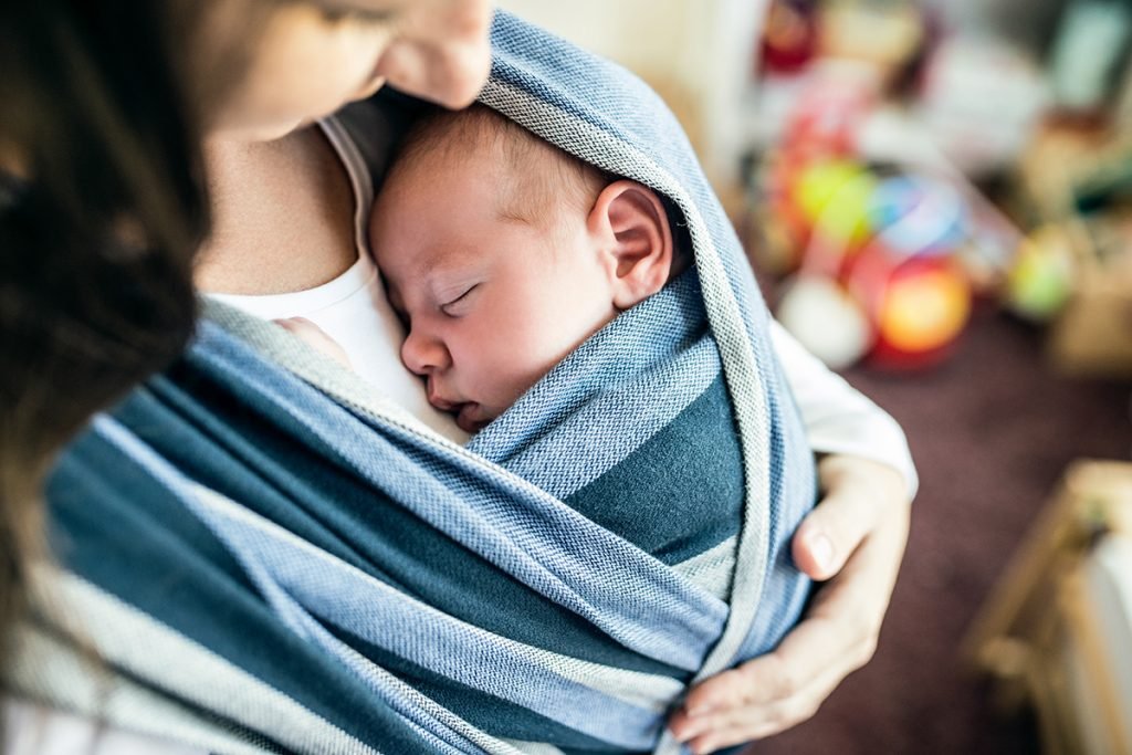 young mother with her newborn baby son in sling at home
