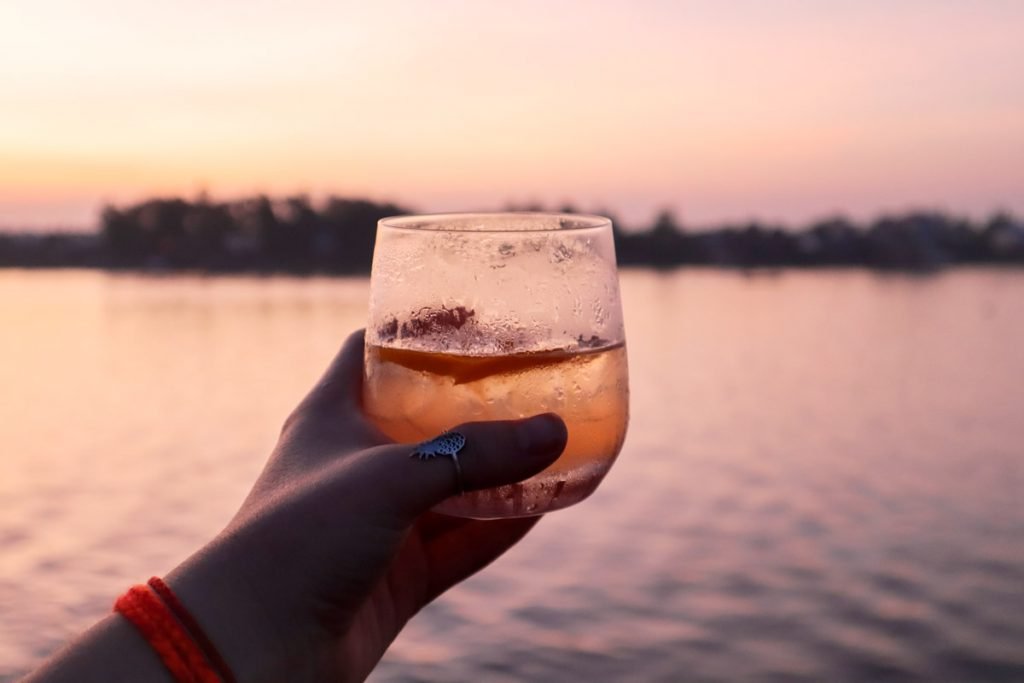 A woman drinks a cocktail at sunset on a cruise ship overlooking the water. 