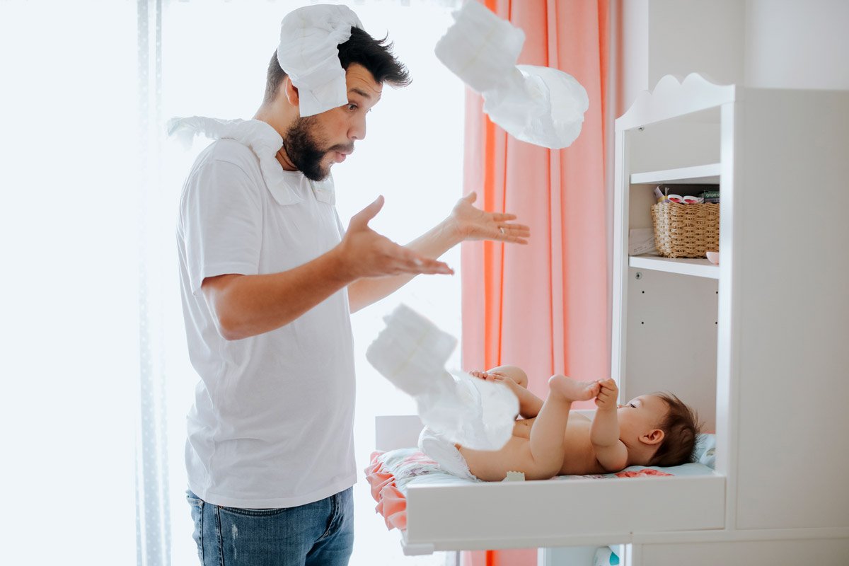 A dad throws diapers in the air as he changes his baby's diaper. 