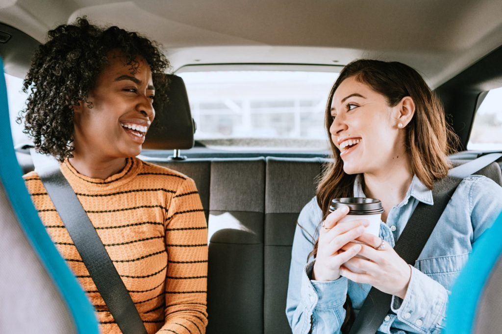 Two women laugh in the backseat of a vehicle.