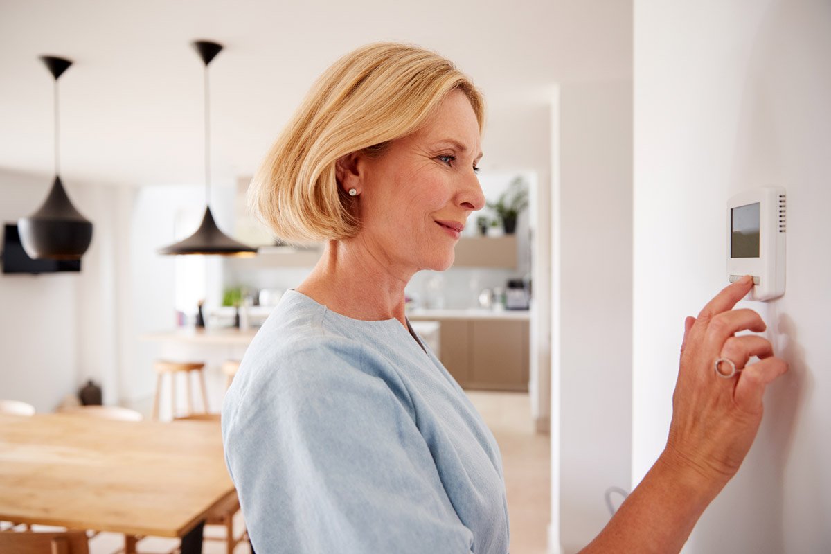 A woman adjusts the thermostat.