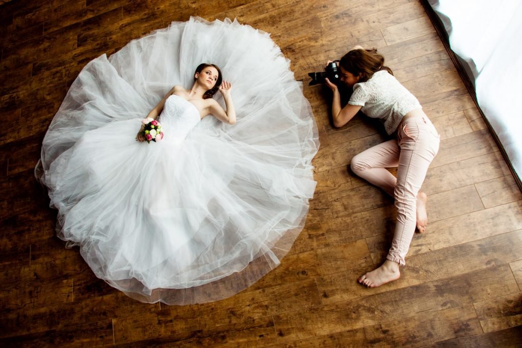 A bride lays down as a photographer takes their portrait.