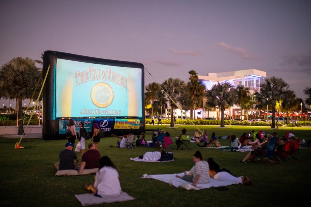 People wait for a free movie to start in a park.