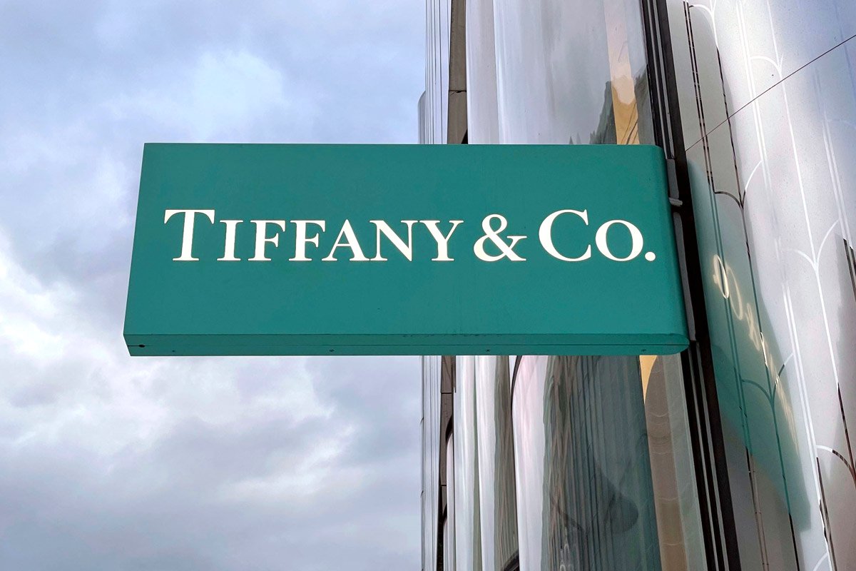 A Tiffany & Co sign hangs outside of the storefront against cloudy skies. 