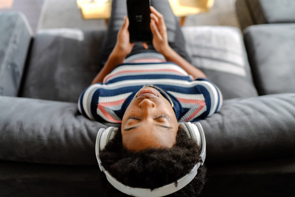 A woman listens to an audio book while reclining on her couch.