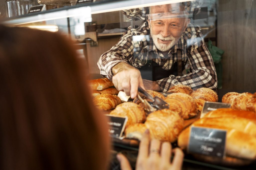 A man takes out a croissant out of a display case for a customer who is purchasing it.