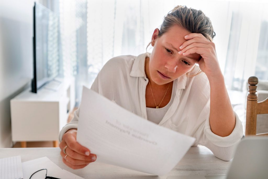 A woman looks stressed out as she looks at a bill at her desk.