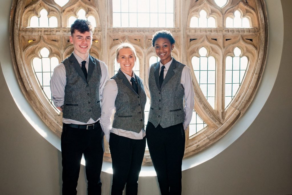Three hotel workers stand by a window in their uniform.