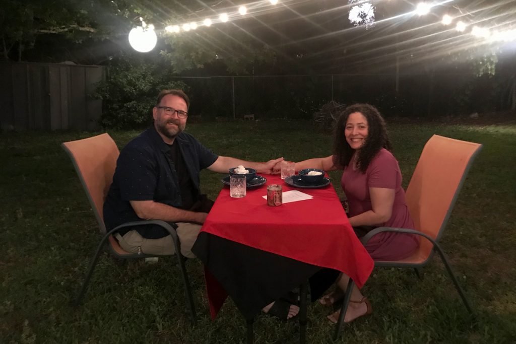A couple hold hands as they enjoy dinner in their backyard.