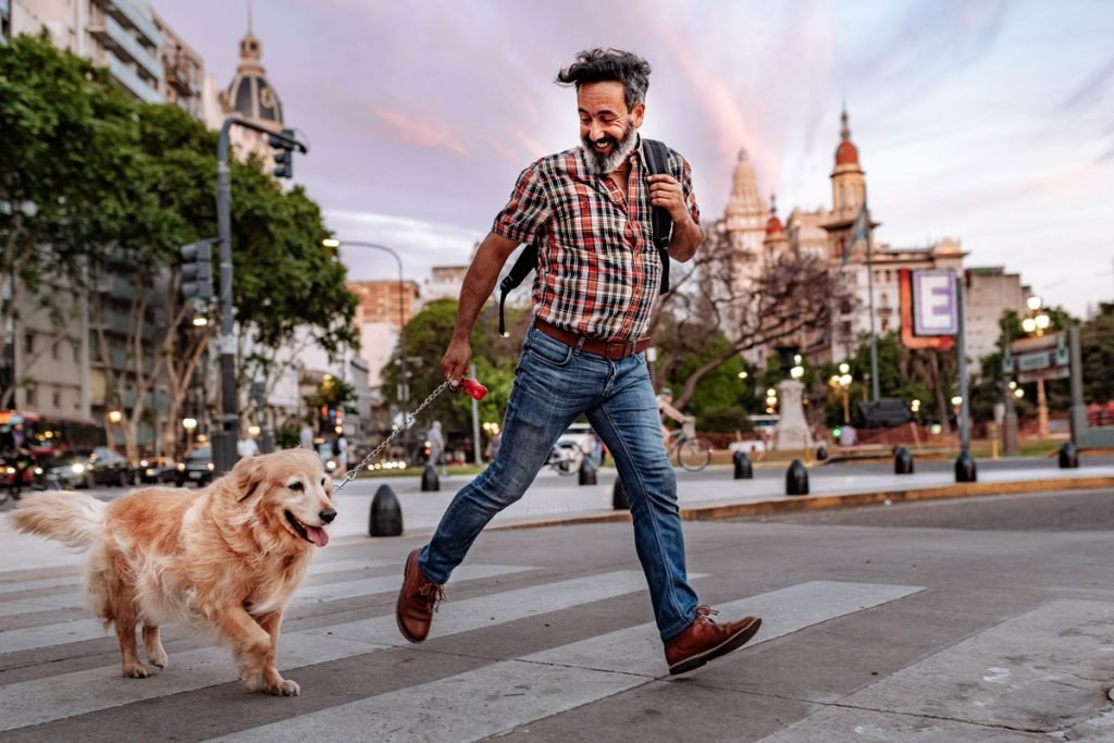 A man runs across a busy street downtown with a golden retriever.