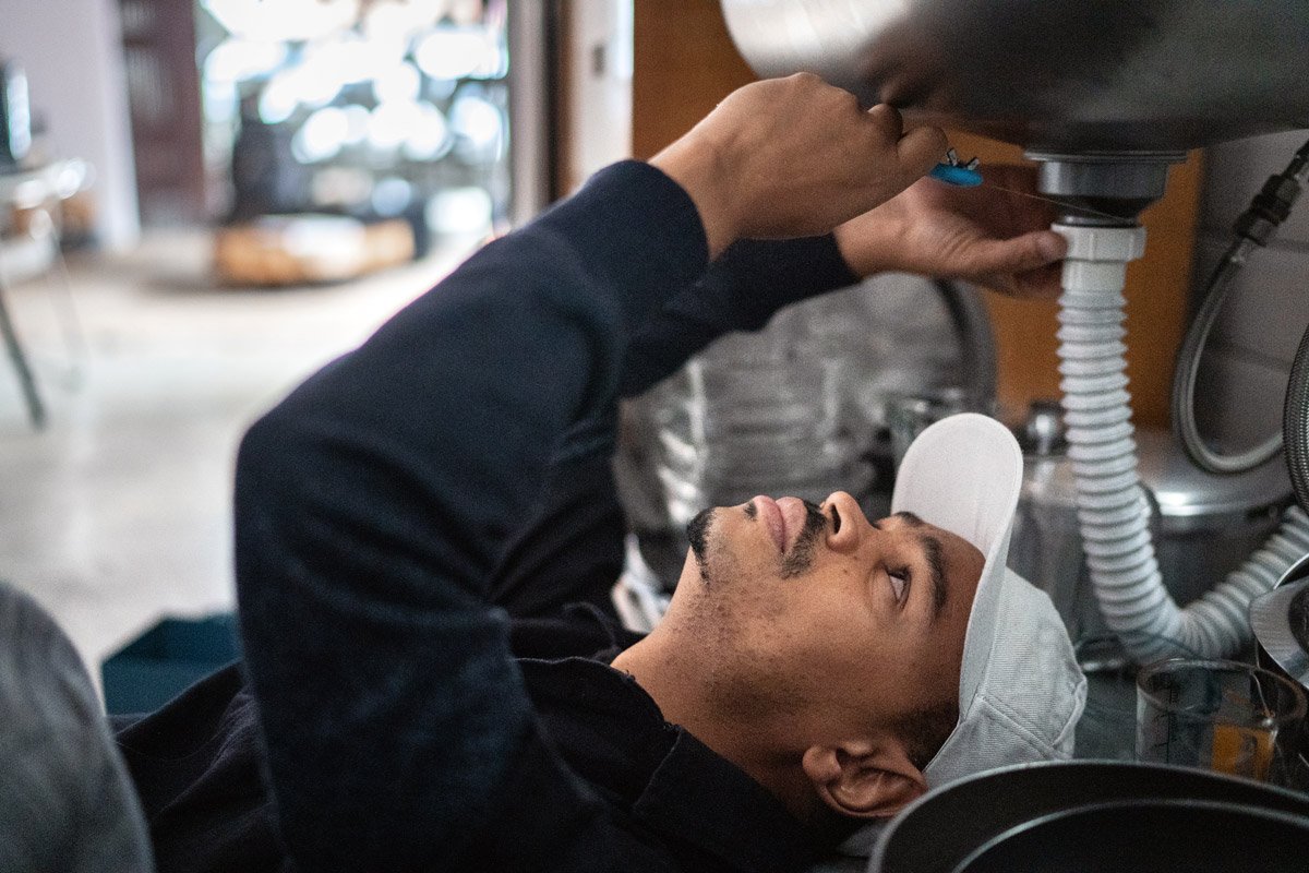 A man fixes a leaky pipe underneath a person's sink.