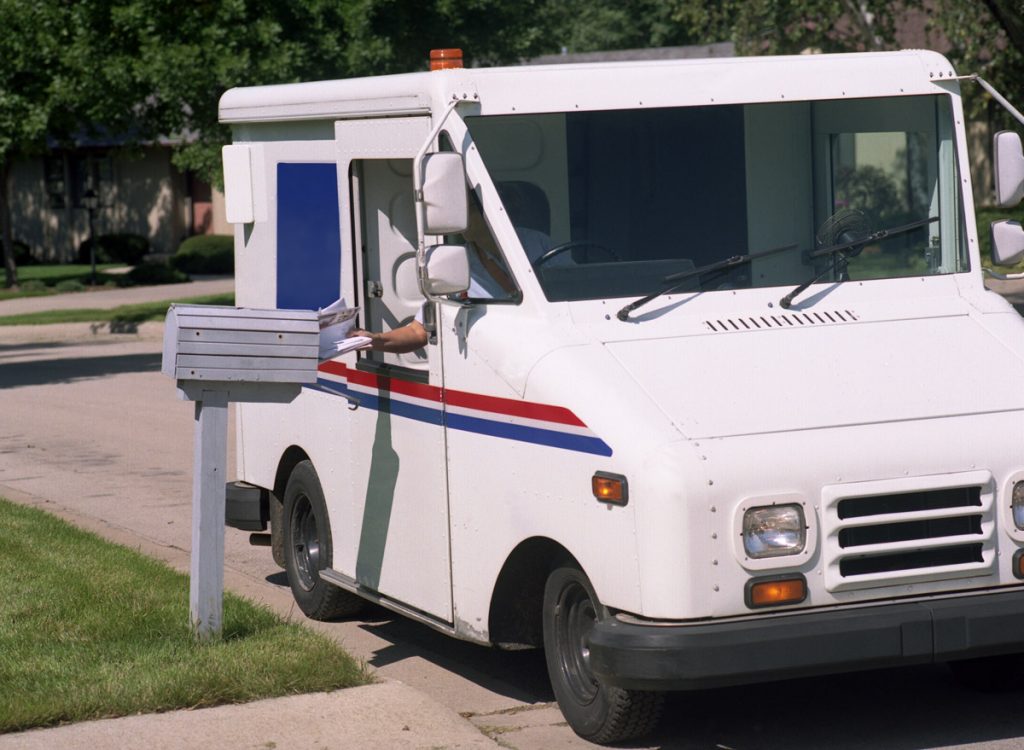 A mail carrier puts a piece of mail in someone's mailbox. 