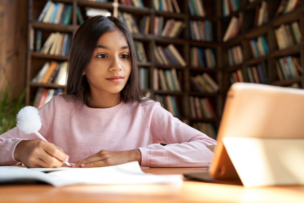 A girl does school work while she listens to her tutor on her iPad.