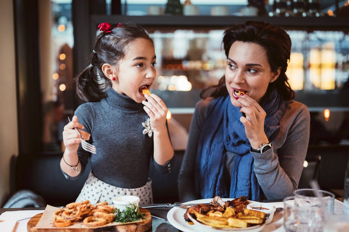 A mother and daughter eat fries and bbq food.