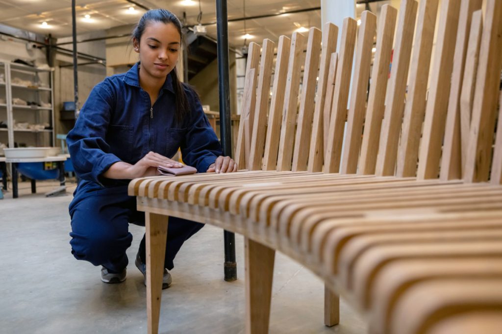 A woman sands down wooden chairs.