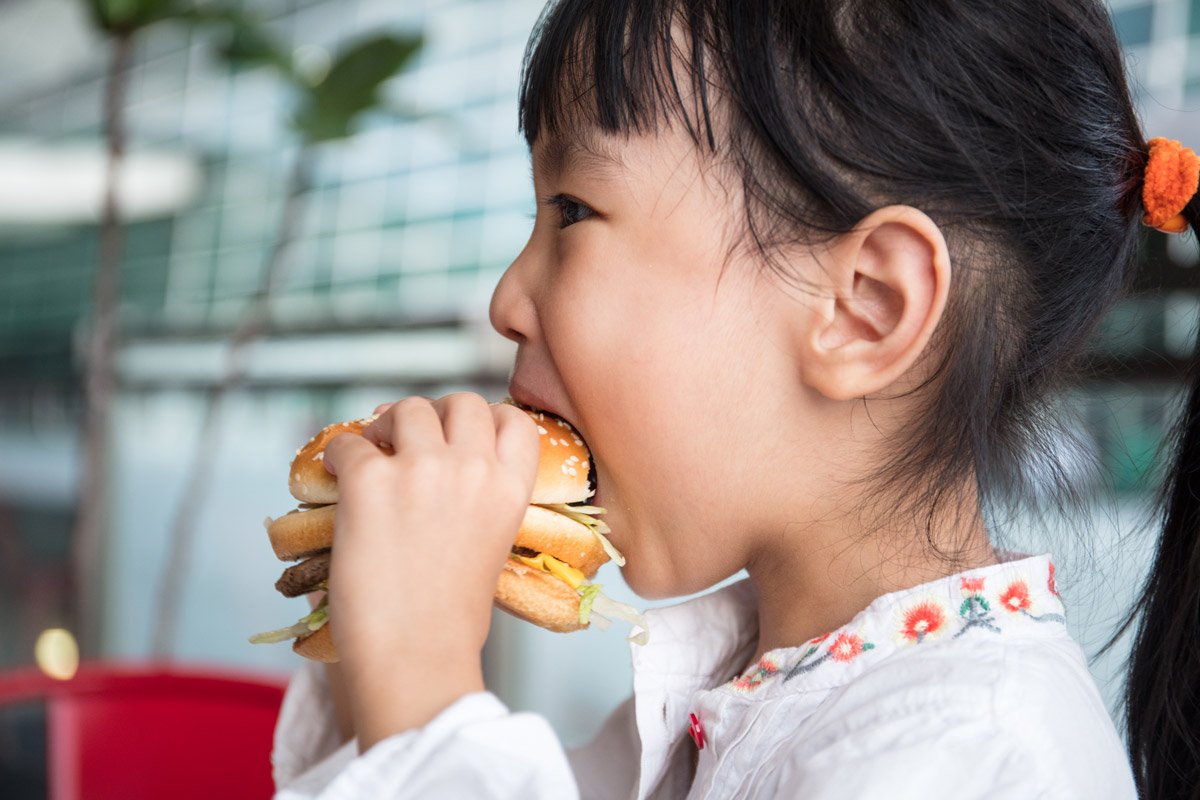 A little girl eats a burger.