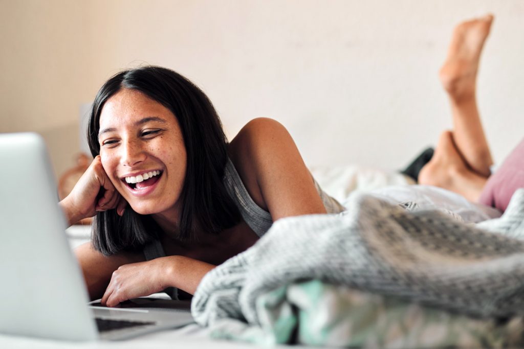 A woman laughs as she works on her laptop from home.
