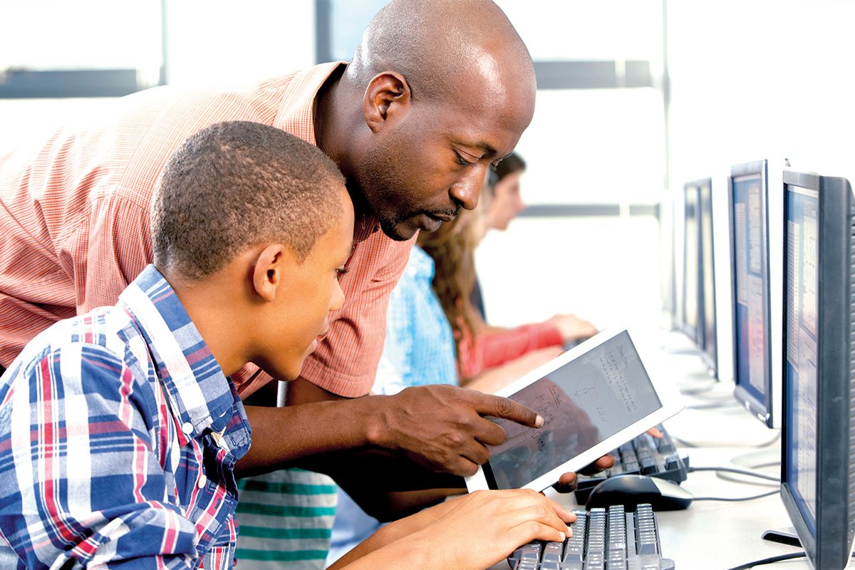 A teacher and students using computers and a touchscreen tablet