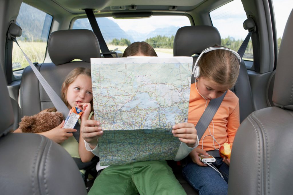 Three sisters sit in the back seat while staring at a road map. 